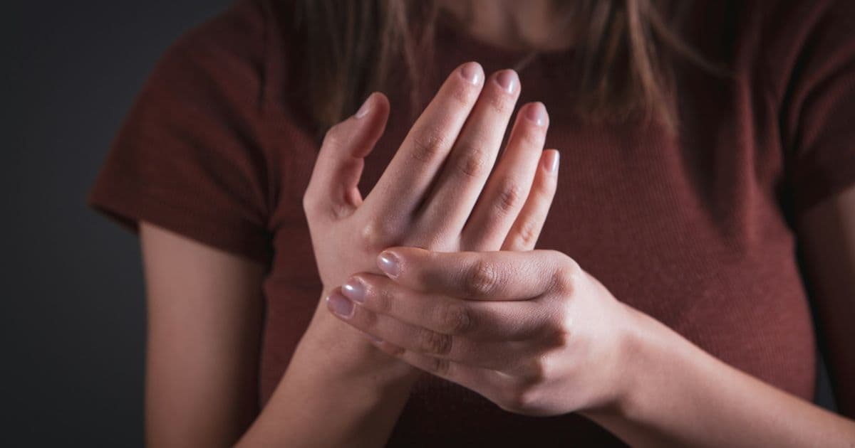 A woman holds her painful hand and wrist, a common early sign of arthritis